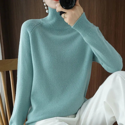 Person wearing a light blue turtleneck sweater and white pants, sitting on a wooden chair.