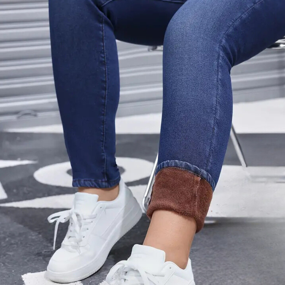 Person wearing blue jeans with rolled-up cuffs and white sneakers on a street.