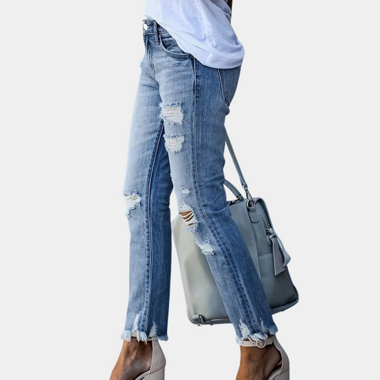 Person wearing ripped blue jeans holding a gray handbag on a light gray background