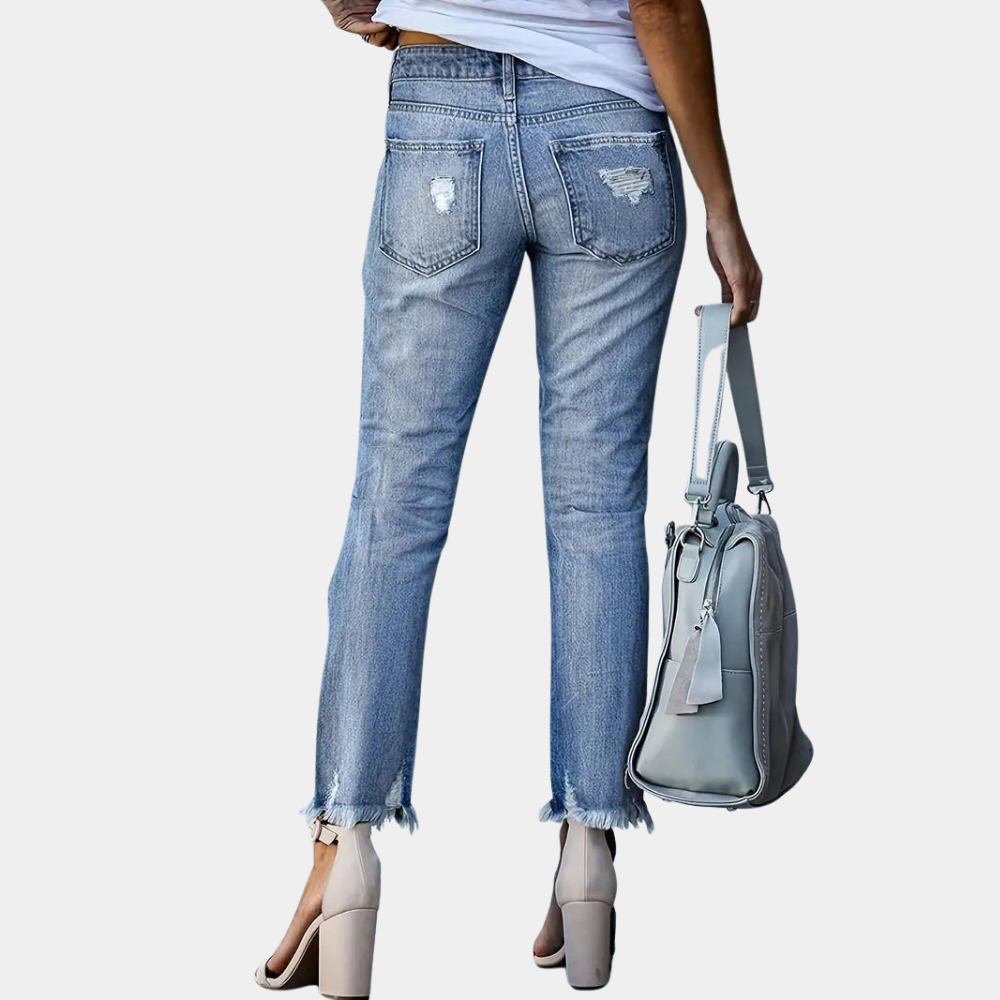 Person wearing light blue jeans holding a gray handbag on a white background