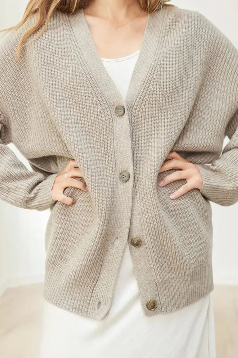 Person wearing a beige knitted cardigan with buttons on a white background