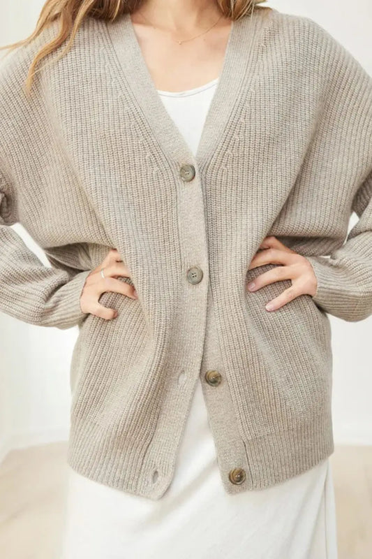 Person wearing a beige knitted cardigan with buttons on a white background