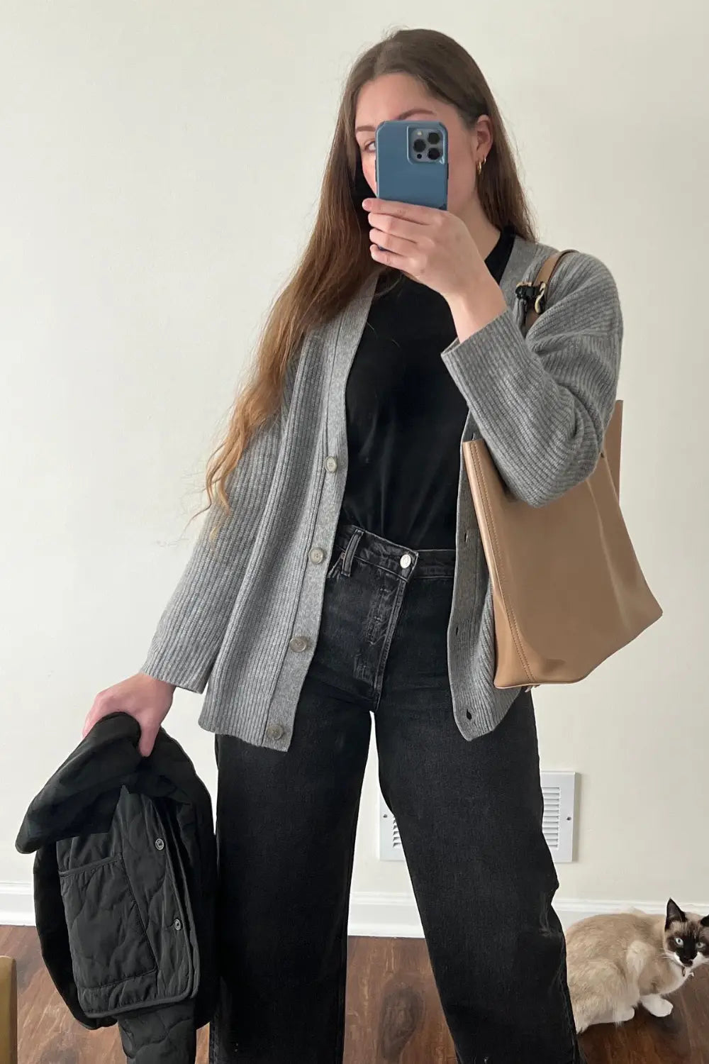 Person taking a mirror selfie wearing a gray cardigan, black shirt, and jeans, holding a beige tote bag.