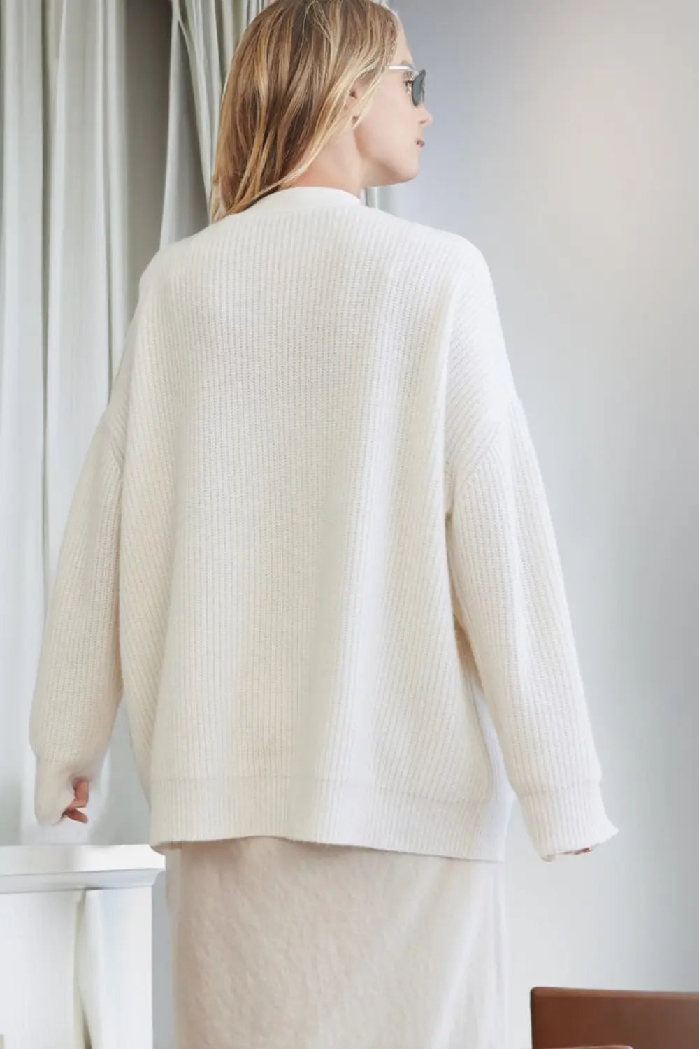 Person wearing a cream ribbed sweater in an indoor setting