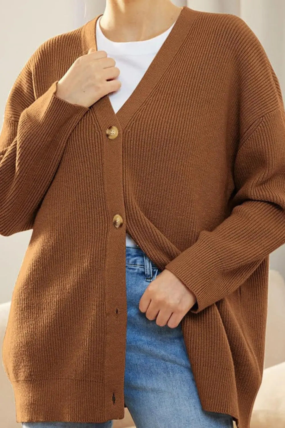 Person wearing a brown cardigan over a white shirt and blue jeans.
