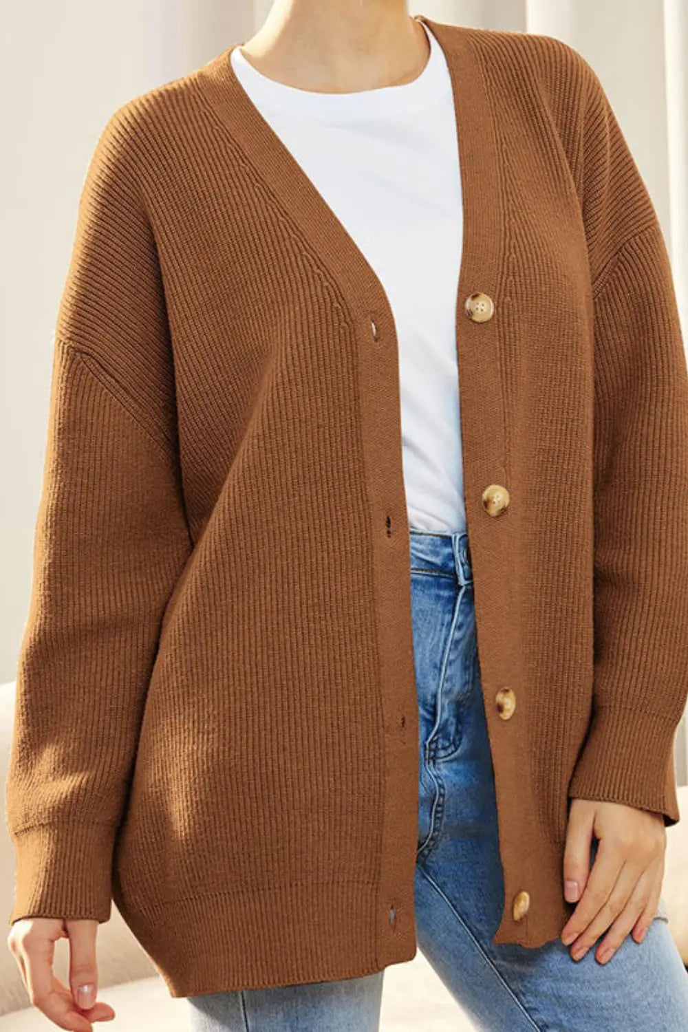 Person wearing a brown cardigan over a white shirt and blue jeans.