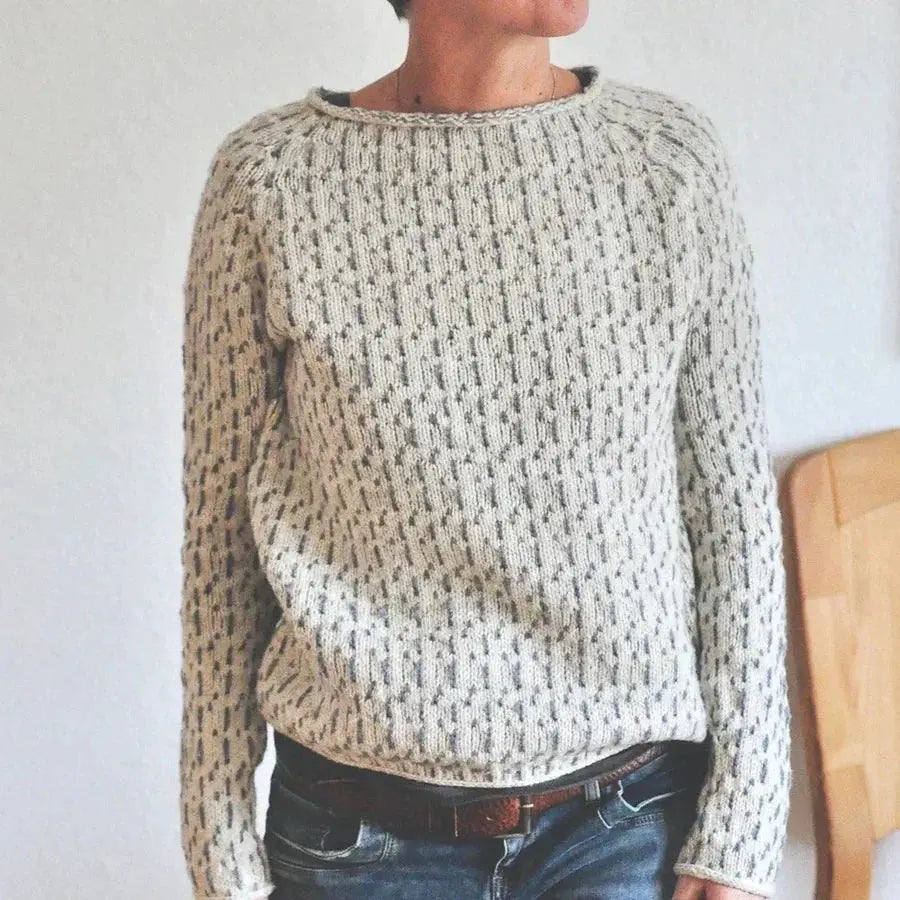 Person wearing a chunky knit sweater with a neutral background