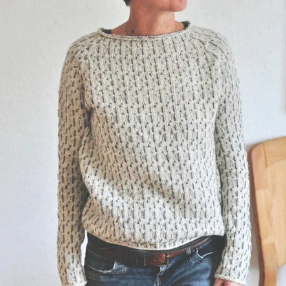 Person wearing a chunky knit sweater with a neutral background