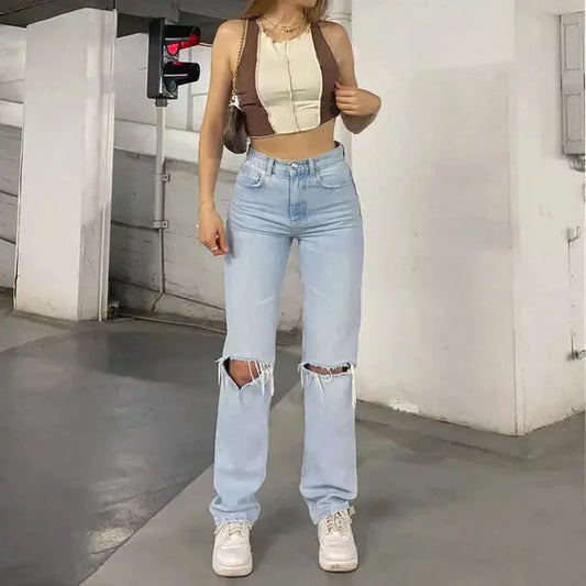Person wearing a beige crop top and light blue ripped jeans in an urban setting.