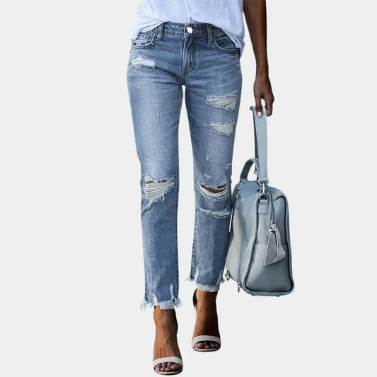 Person wearing distressed blue jeans and holding a gray handbag on a white background