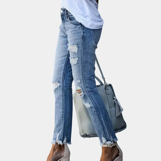 Person wearing ripped blue jeans holding a gray handbag on a light gray background