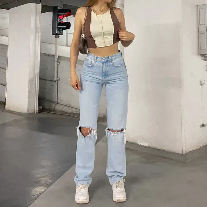 Person wearing a beige crop top and light blue ripped jeans in an urban setting.