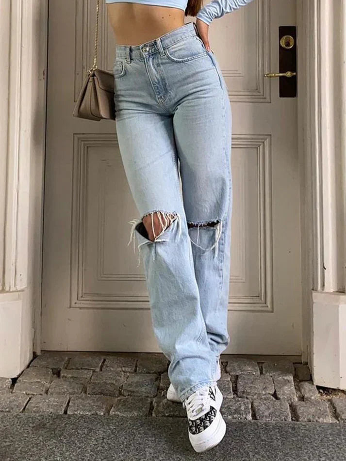 Person wearing light blue ripped jeans standing in front of a door.