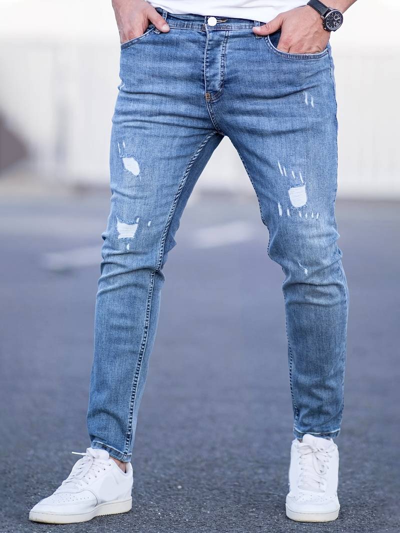 Person wearing distressed blue jeans and white sneakers on a blurred background