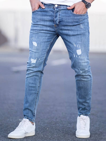 Person wearing distressed blue jeans and white sneakers on a blurred background