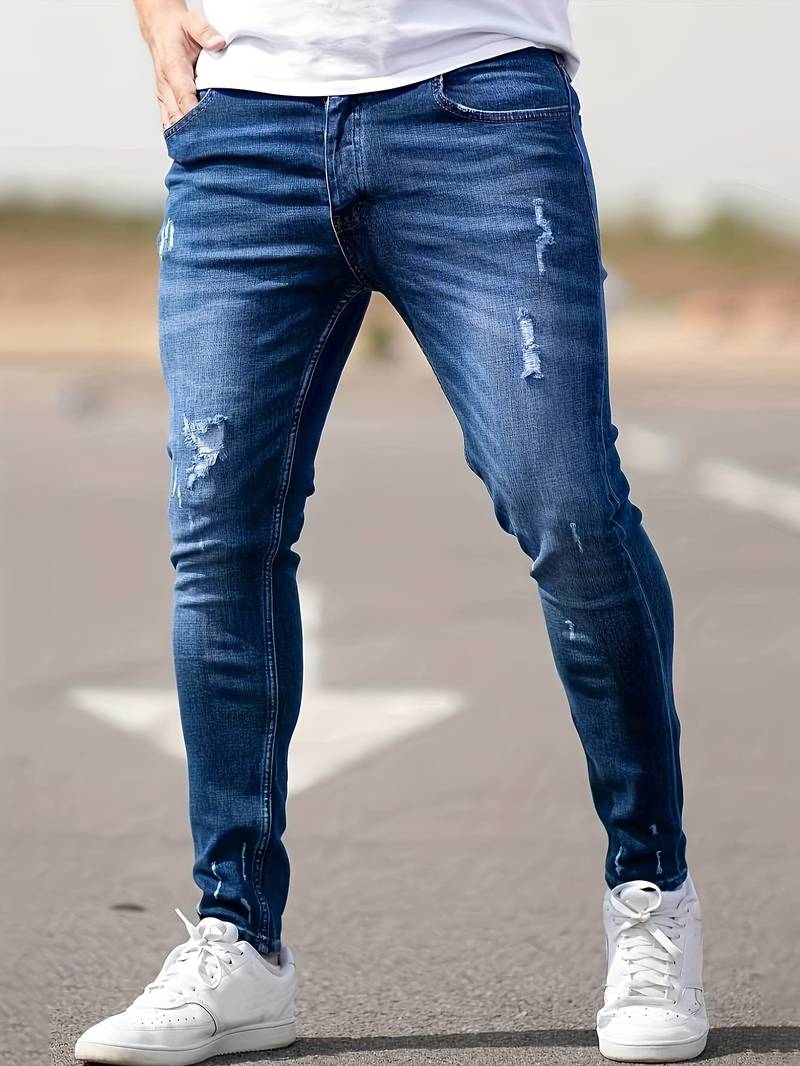 Person wearing blue jeans and white sneakers on a road.