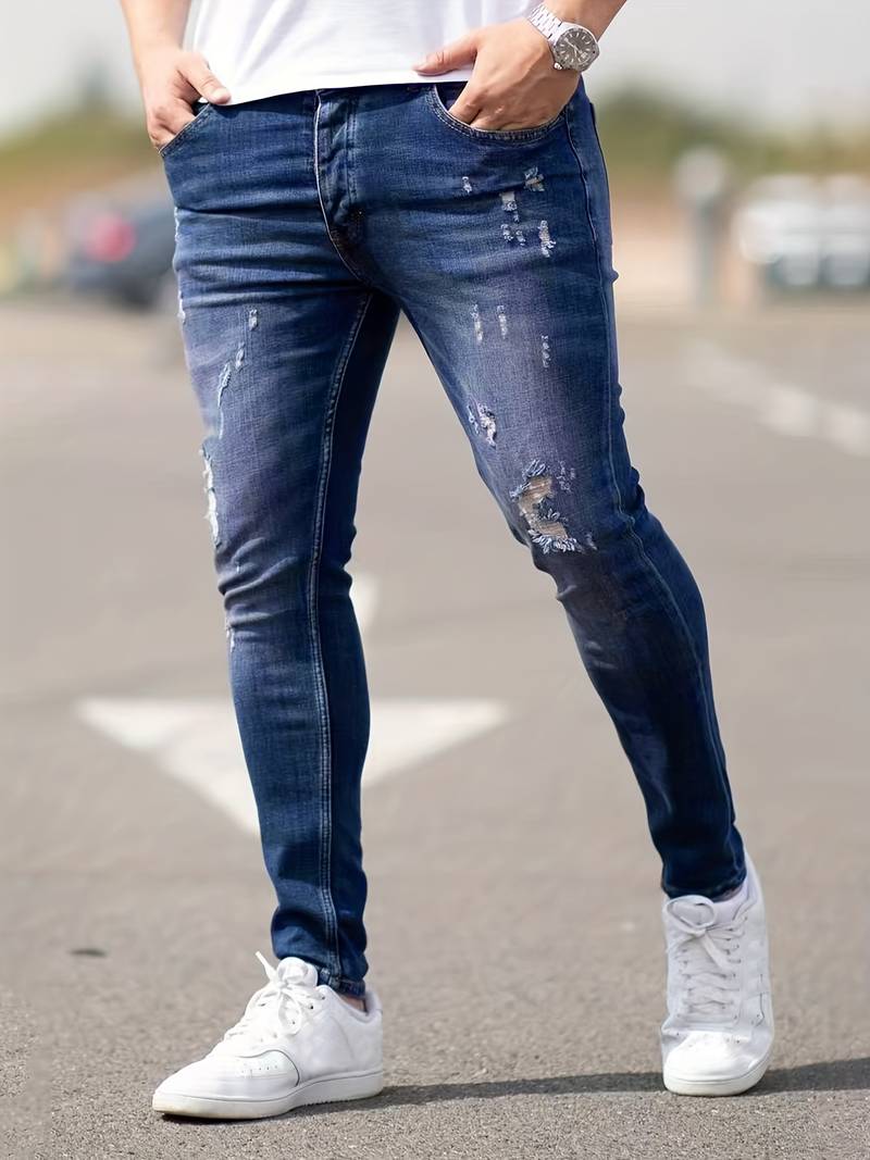 Person wearing distressed blue jeans and white sneakers on a road.