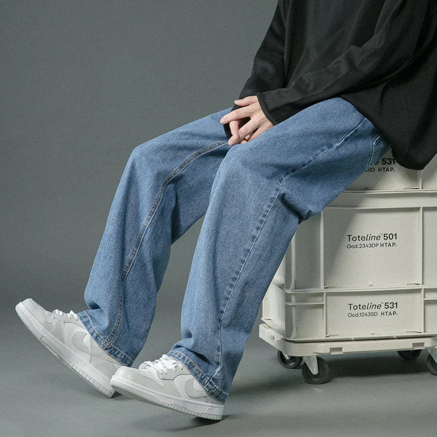 Person wearing blue jeans and white sneakers sitting on a crate against a gray background