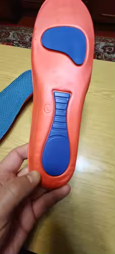 Orange insole with blue accents held by a hand on a wooden surface